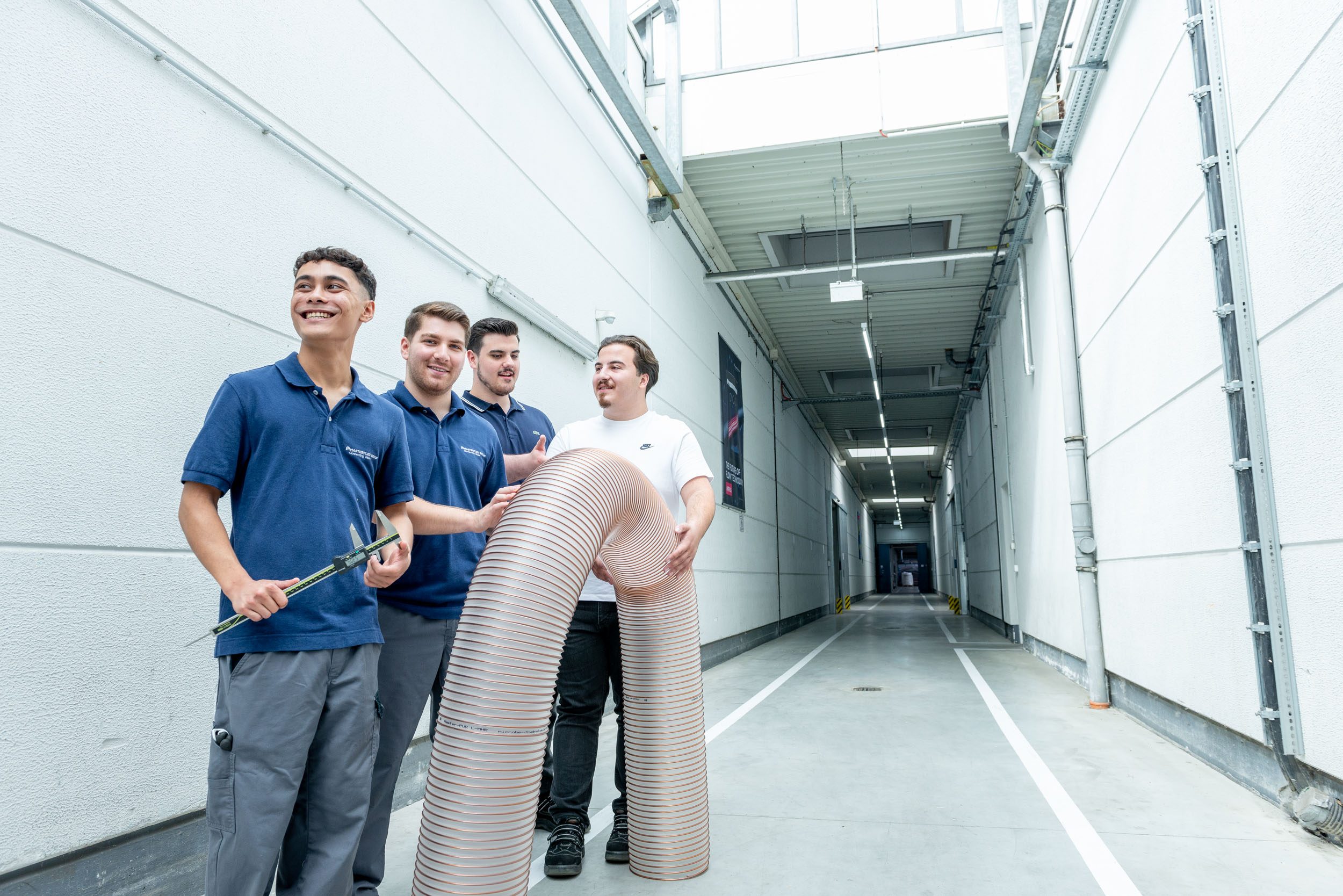 Azubis stehen gemeinsam mit einem Schlauch in der Produktionshalle