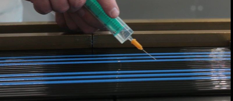 You can see a syringe with liquid, an adhesive agent, which is directed onto small high-purity plastic tubes and apparently connects these tube elements together to create a multiple tube for semiconductor technologies