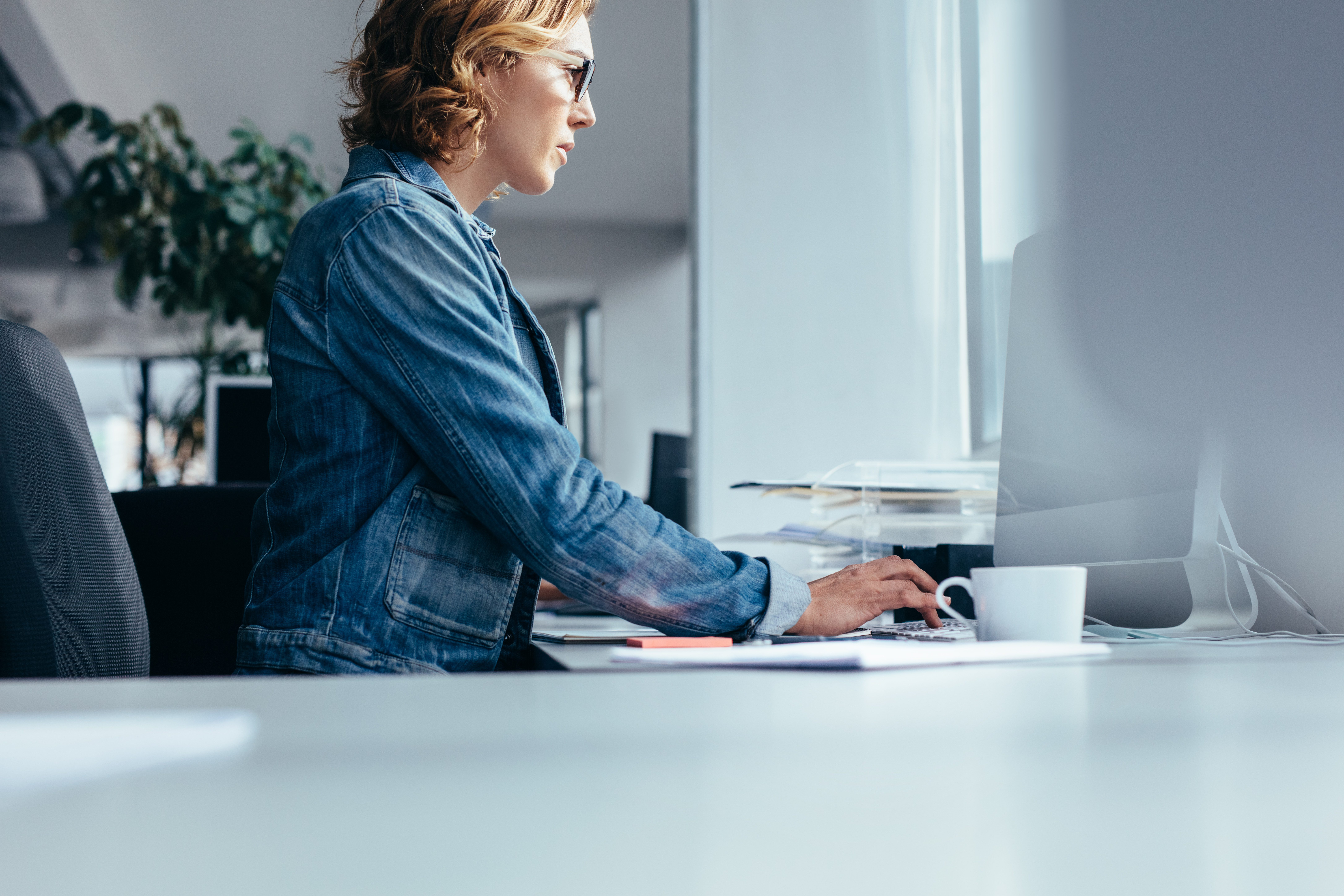 Woman sitting in front of PC with coffee cup.