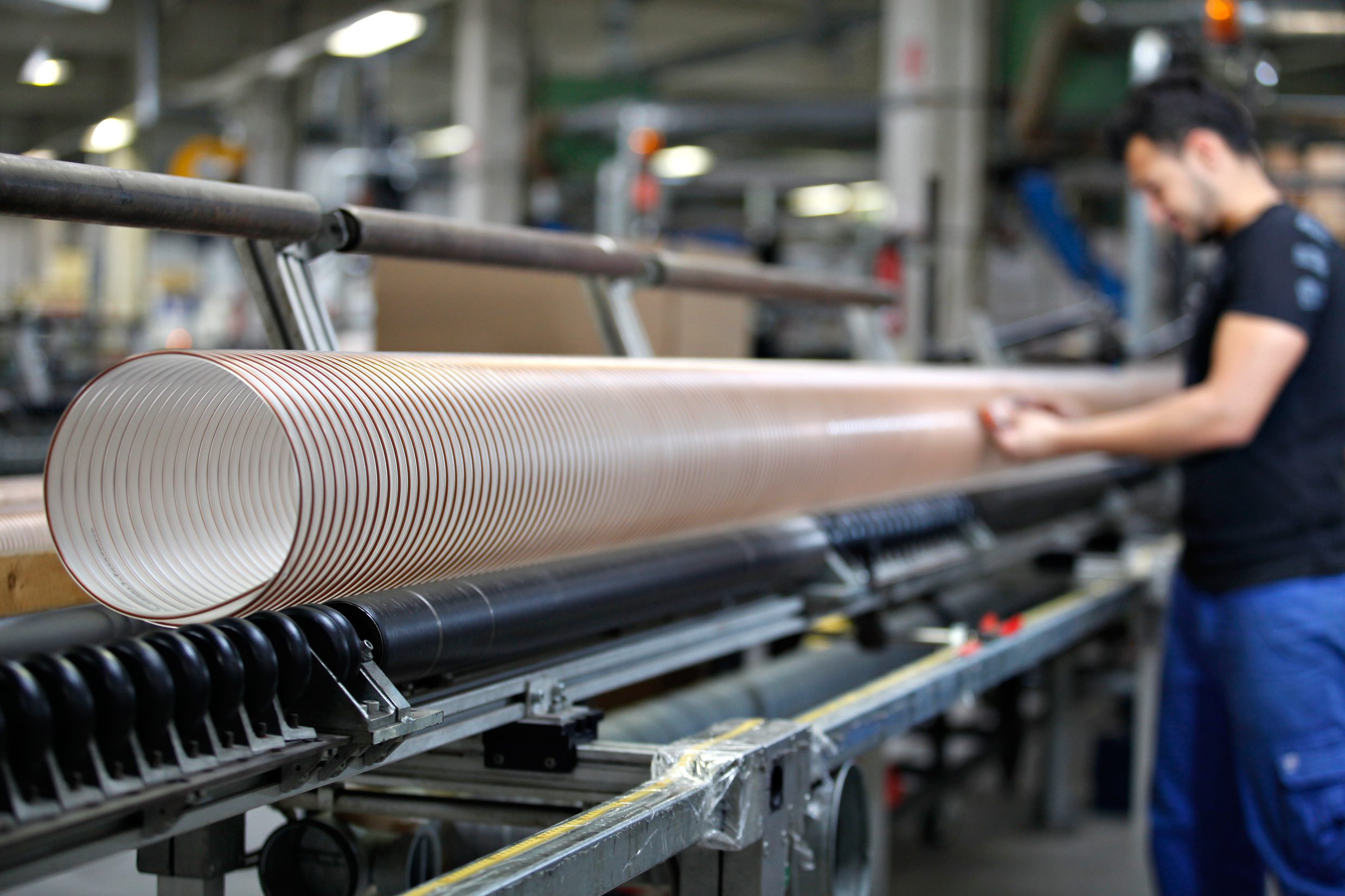 A production worker stands at a machine and produces a hose. 