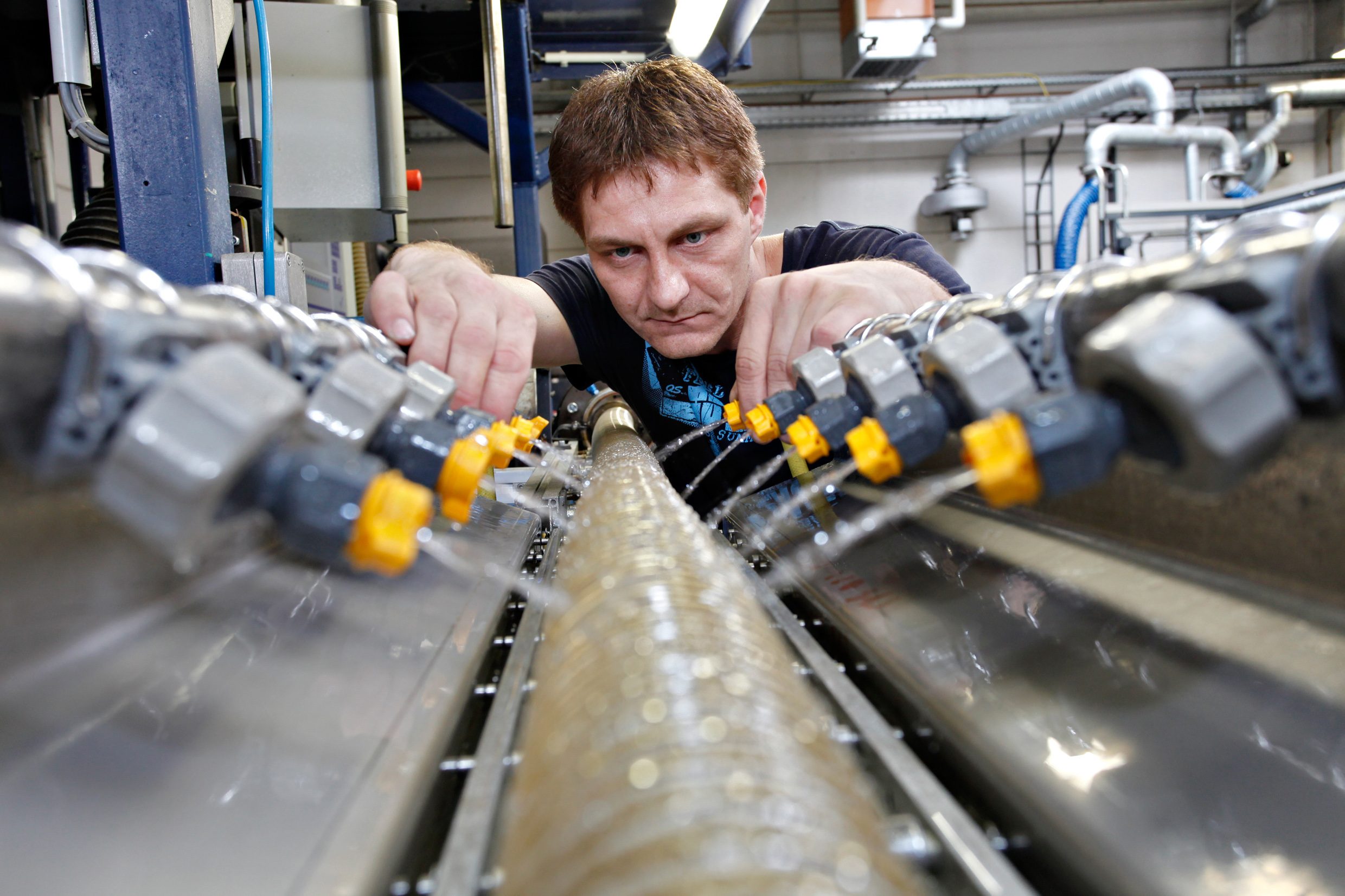 An employee at the production machine cools the hose that has just been produced and is still hot with water flowing from small nozzles. 
