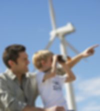 Masterflex Group Responsibility in Society A man kneels with his son, who looks into the distance with binoculars, in front of a wind turbine.