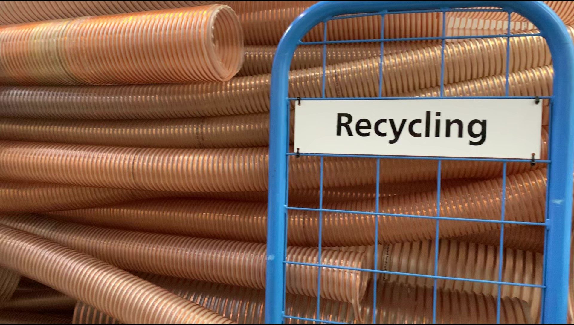 Es liegen extrudierte Schlauchabfälle in unterschiedlichen Größen auf einem Wagen, der zur Recyclingstation gefahren wird. Der Wagen ist mit einem Schild 