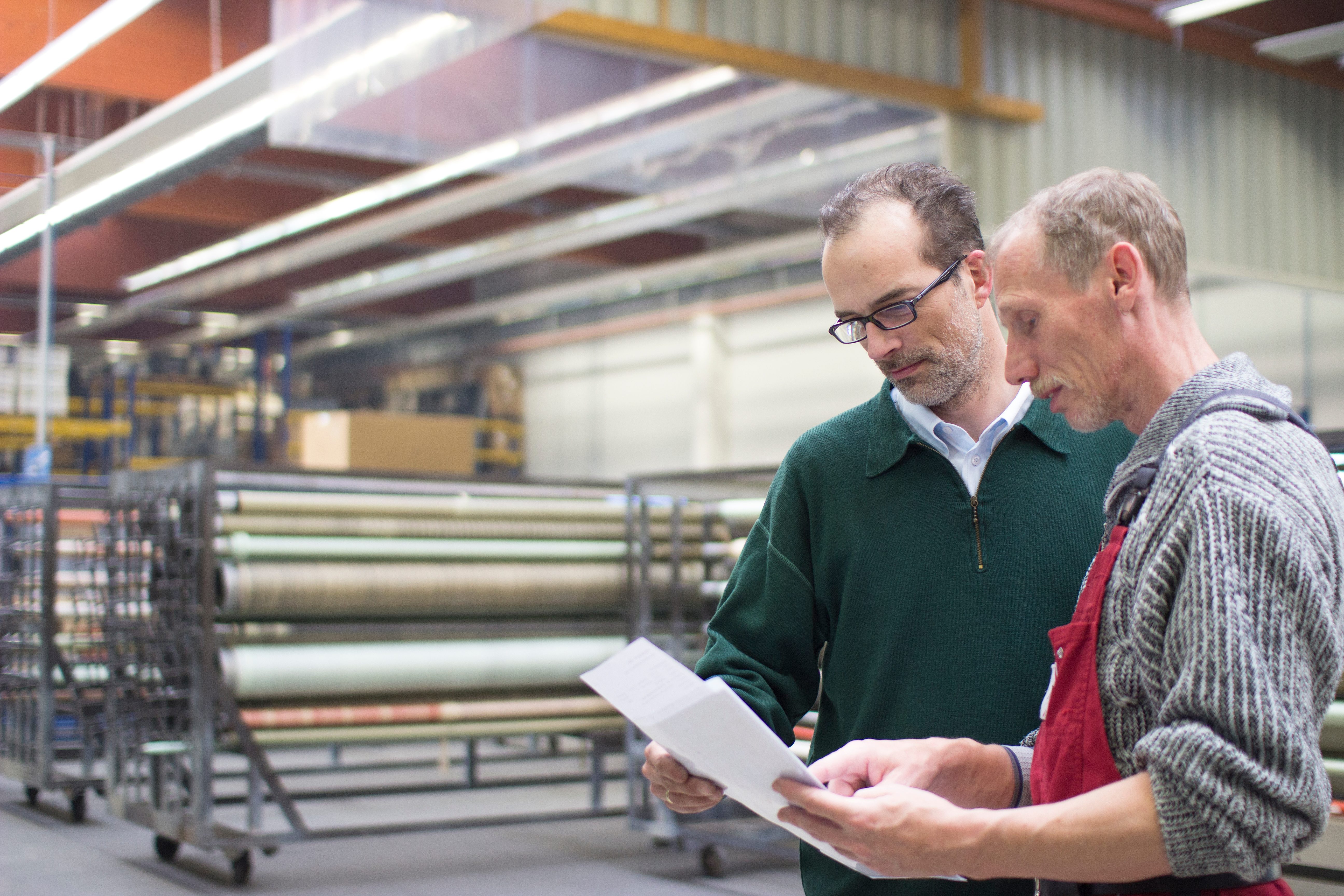 Two colleagues from Matzen & Timm stand in the production area and look together at a technical drawing.