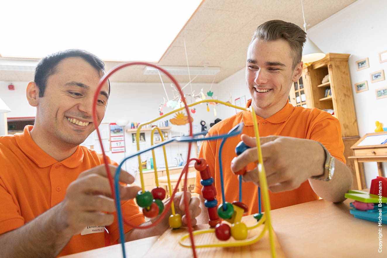 2 lächelnde Auszubildende beim Girls Day 2019 im Kindergarten spielen mit einem Motorikgerät für Kinder.